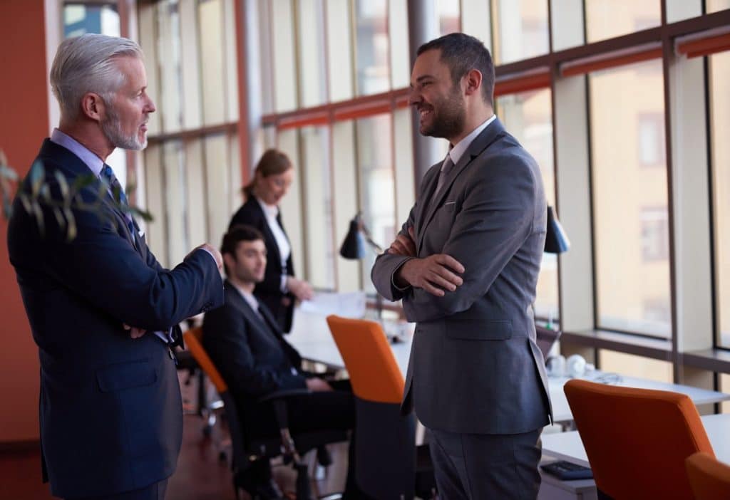 middle-aged man wearing a suit talking to a younger man wearing a suit