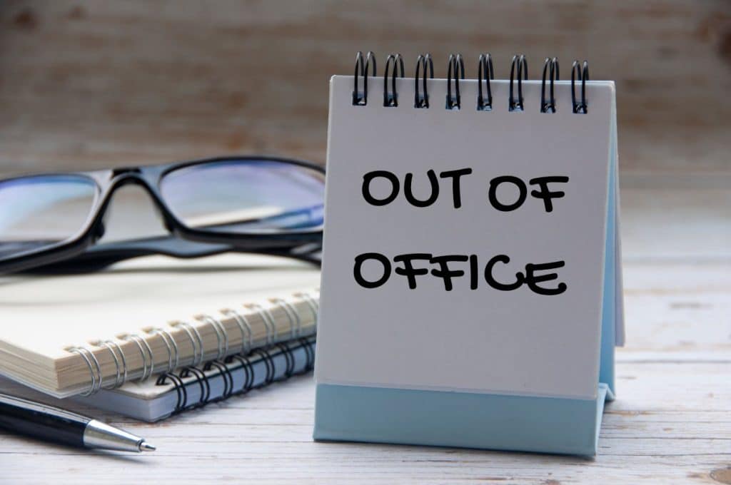 Out of office text on calendar desk with notebook and glasses background
